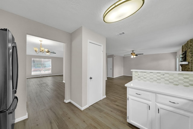 kitchen featuring white cabinetry, pendant lighting, stainless steel fridge, and light hardwood / wood-style flooring