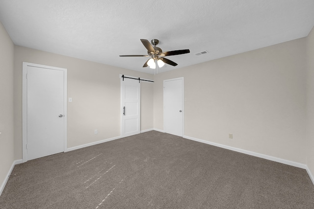 unfurnished bedroom with ceiling fan, a barn door, carpet, and a textured ceiling