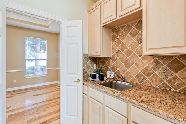 kitchen featuring light stone countertops, light brown cabinetry, light wood-type flooring, tasteful backsplash, and sink