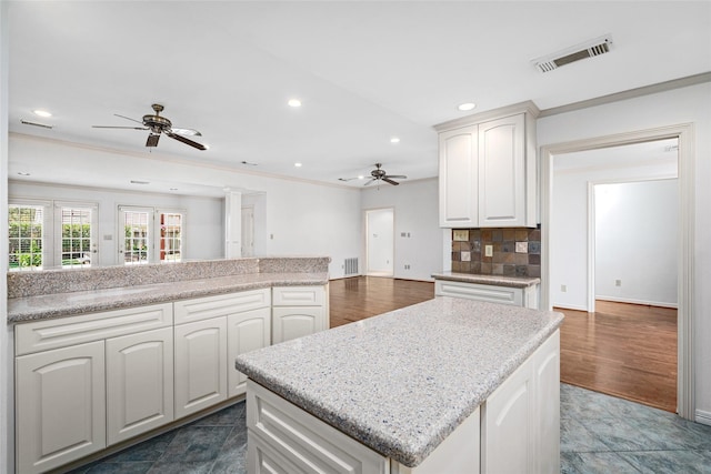 kitchen with white cabinets, a center island, tasteful backsplash, ornamental molding, and ceiling fan