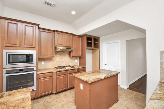 kitchen featuring lofted ceiling, stainless steel appliances, a kitchen island, light stone countertops, and decorative backsplash