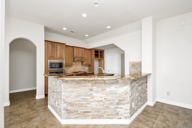 kitchen with stainless steel appliances, backsplash, light stone counters, and kitchen peninsula