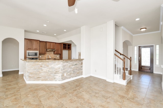 kitchen featuring kitchen peninsula, light stone countertops, sink, stainless steel microwave, and decorative backsplash