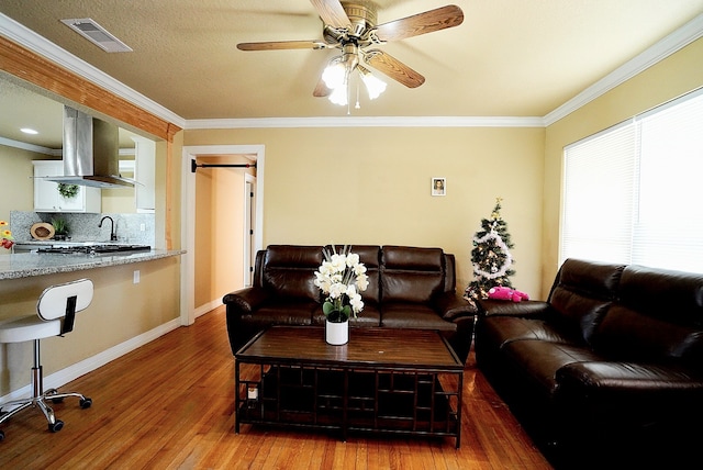 living room featuring ceiling fan, sink, wood-type flooring, and crown molding