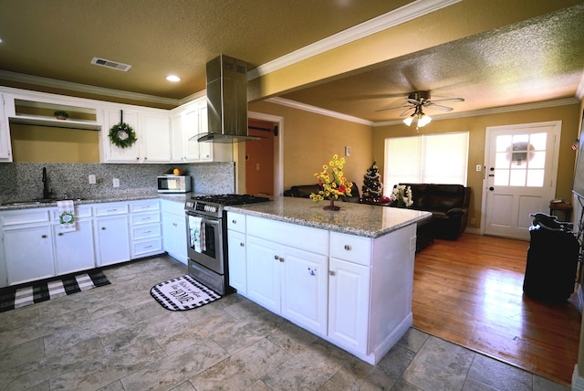 kitchen featuring kitchen peninsula, wall chimney exhaust hood, stainless steel gas stove, stone countertops, and white cabinetry