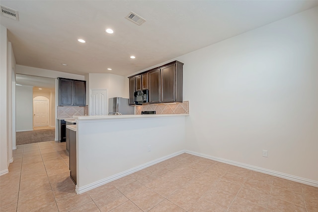 kitchen with kitchen peninsula, stainless steel fridge, tasteful backsplash, and dark brown cabinets