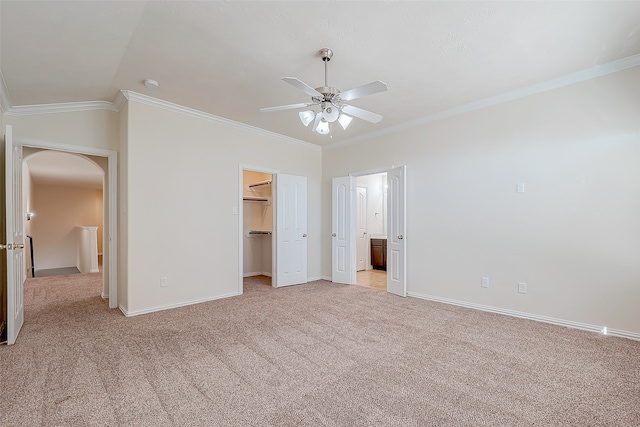 unfurnished bedroom with ceiling fan, crown molding, lofted ceiling, a walk in closet, and light carpet