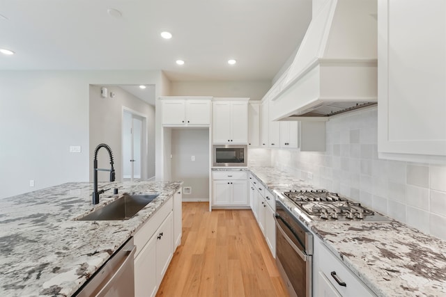 kitchen with white cabinetry, sink, light stone countertops, premium range hood, and light wood-type flooring