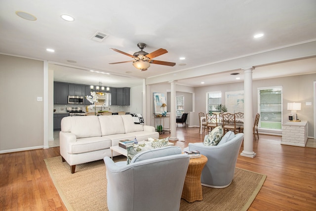 living room with ornamental molding, ceiling fan with notable chandelier, and light wood-type flooring