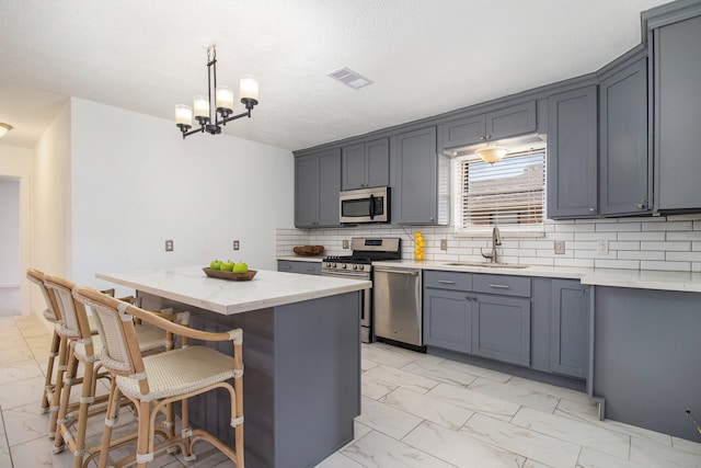 kitchen featuring gray cabinetry, sink, hanging light fixtures, appliances with stainless steel finishes, and a kitchen island