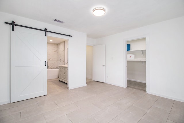 unfurnished bedroom featuring ensuite bath, a barn door, a walk in closet, a closet, and light tile patterned floors