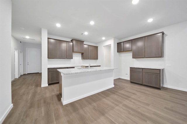 kitchen featuring a kitchen island with sink, sink, hardwood / wood-style flooring, light stone countertops, and dark brown cabinets