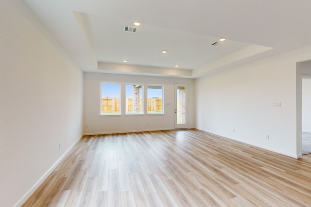 spare room with a raised ceiling and light wood-type flooring