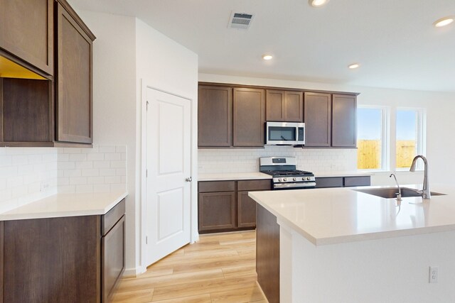 kitchen featuring sink, stainless steel appliances, tasteful backsplash, dark brown cabinets, and light wood-type flooring