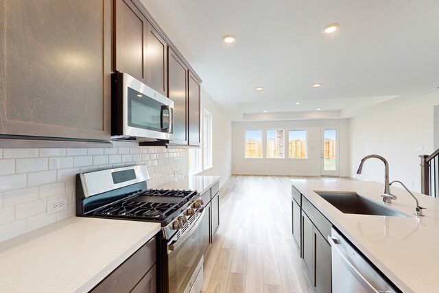 kitchen featuring sink, stainless steel appliances, light hardwood / wood-style flooring, backsplash, and dark brown cabinets