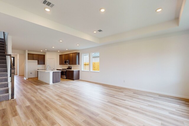 unfurnished living room featuring a tray ceiling, light hardwood / wood-style flooring, and sink