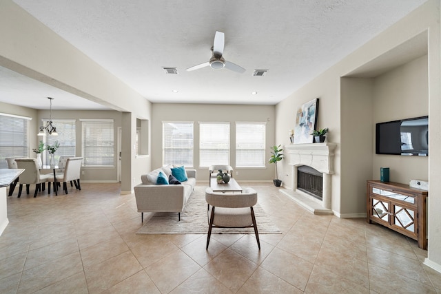 tiled living room with a textured ceiling, a wealth of natural light, and ceiling fan with notable chandelier