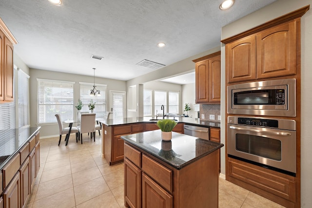 kitchen with a center island, backsplash, hanging light fixtures, dark stone countertops, and stainless steel appliances