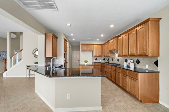 kitchen with stainless steel gas stovetop, backsplash, dark stone counters, sink, and kitchen peninsula