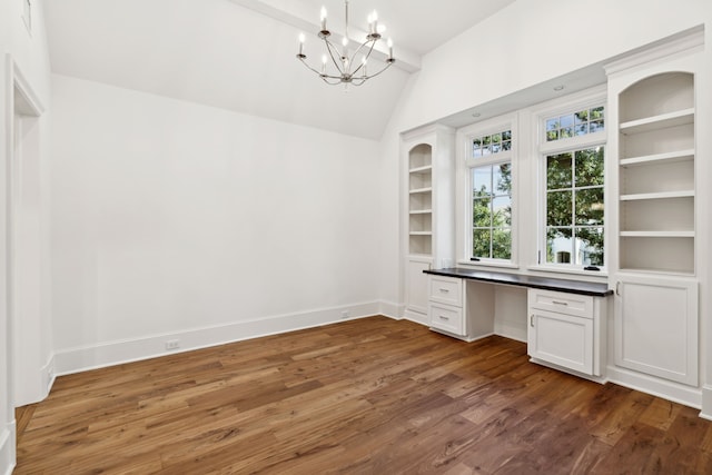 unfurnished office featuring dark wood-type flooring, an inviting chandelier, built in desk, vaulted ceiling, and built in features