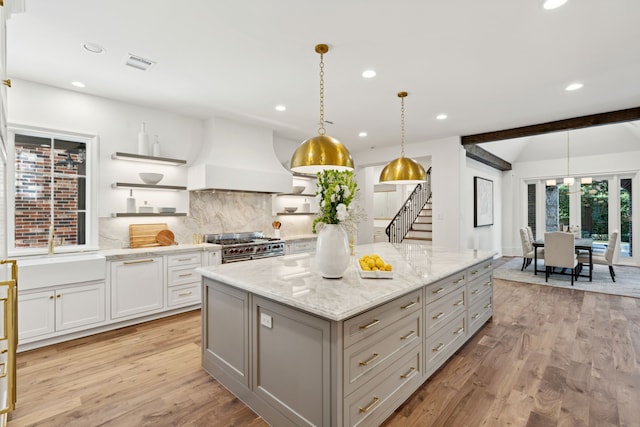 kitchen featuring hanging light fixtures, light hardwood / wood-style floors, a kitchen island, custom exhaust hood, and range with two ovens