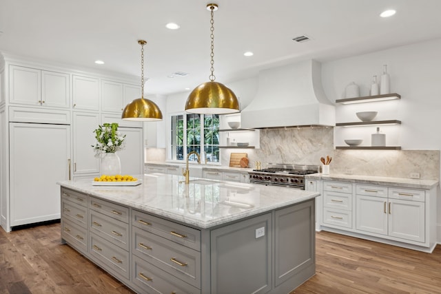 kitchen featuring a kitchen island with sink, white cabinets, range with two ovens, and premium range hood