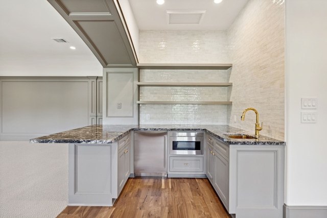 kitchen featuring sink, stainless steel oven, kitchen peninsula, dark stone counters, and light wood-type flooring