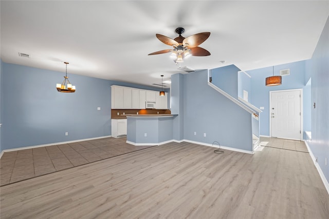 unfurnished living room with ceiling fan with notable chandelier and light hardwood / wood-style flooring