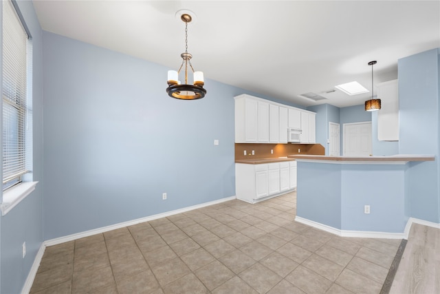 kitchen featuring kitchen peninsula, white cabinets, hanging light fixtures, and an inviting chandelier