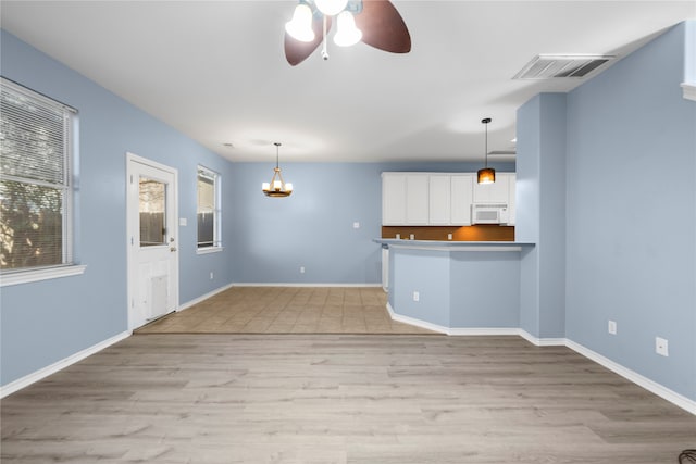 unfurnished living room with ceiling fan with notable chandelier and light wood-type flooring