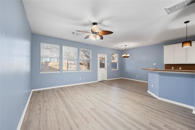 unfurnished living room with ceiling fan with notable chandelier and light wood-type flooring