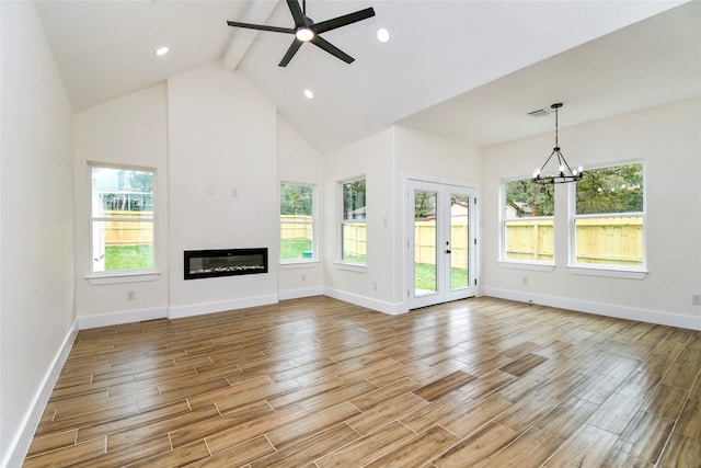 unfurnished living room with a wealth of natural light, beamed ceiling, ceiling fan with notable chandelier, and light wood-type flooring