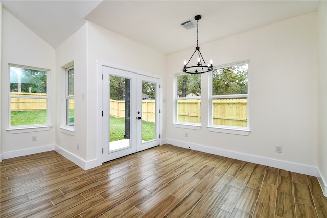 unfurnished dining area with hardwood / wood-style floors, vaulted ceiling, french doors, and a notable chandelier