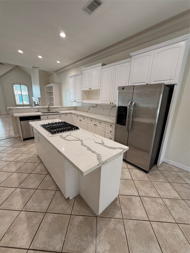 kitchen with light stone countertops, appliances with stainless steel finishes, ornamental molding, a center island, and white cabinetry