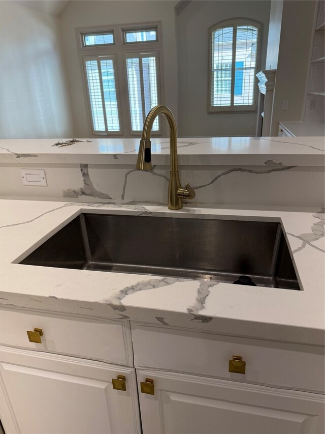 interior details with white cabinets, light stone counters, and sink