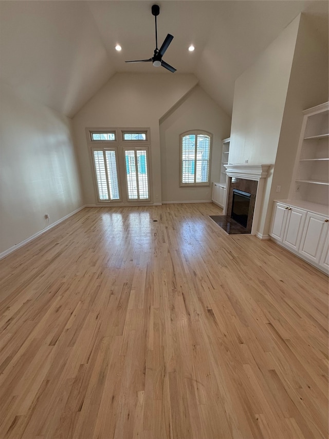 unfurnished living room featuring vaulted ceiling, ceiling fan, built in shelves, a fireplace, and light hardwood / wood-style floors