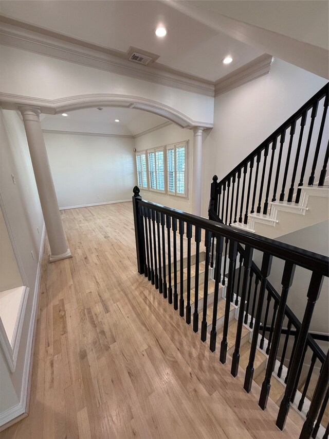 hallway featuring light hardwood / wood-style floors, ornate columns, and crown molding