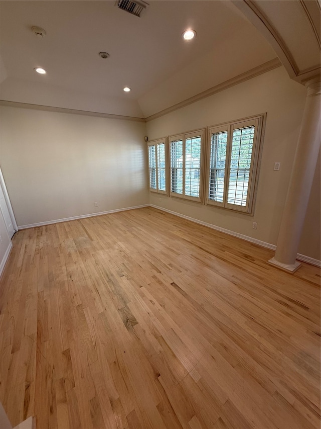 empty room featuring light hardwood / wood-style floors, ornate columns, and vaulted ceiling