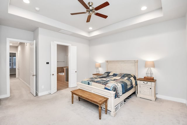 bedroom with ceiling fan, ensuite bathroom, light carpet, and a tray ceiling