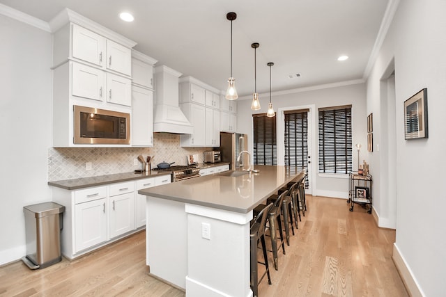 kitchen featuring built in microwave, an island with sink, pendant lighting, a breakfast bar area, and white cabinets