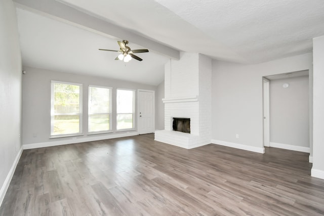 unfurnished living room with vaulted ceiling with beams, ceiling fan, wood-type flooring, and a brick fireplace