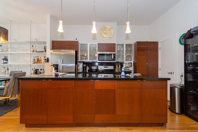 kitchen with a kitchen island with sink, pendant lighting, light hardwood / wood-style floors, and appliances with stainless steel finishes