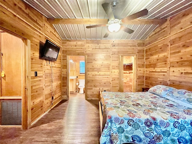 bedroom with wooden walls, ceiling fan, connected bathroom, beam ceiling, and wood-type flooring