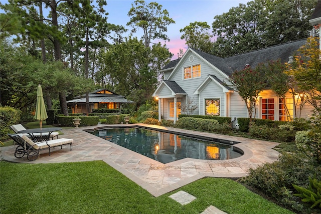 pool at dusk featuring a patio and a lawn