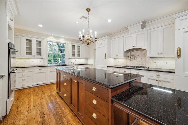 kitchen with decorative light fixtures, white cabinetry, a center island with sink, and light hardwood / wood-style floors