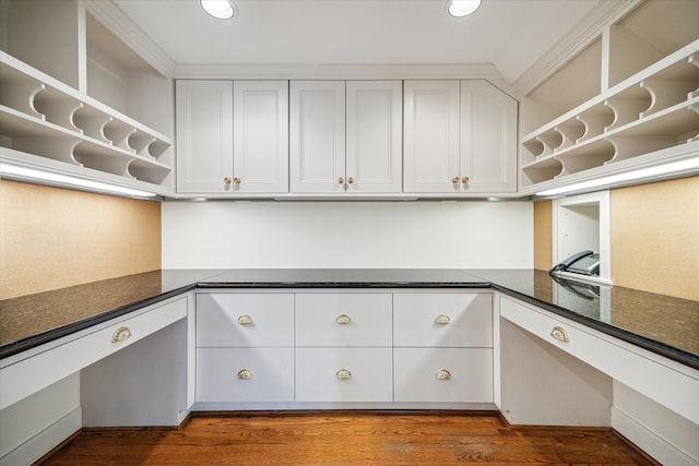 kitchen with white cabinets, dark hardwood / wood-style floors, ornamental molding, and dark stone counters