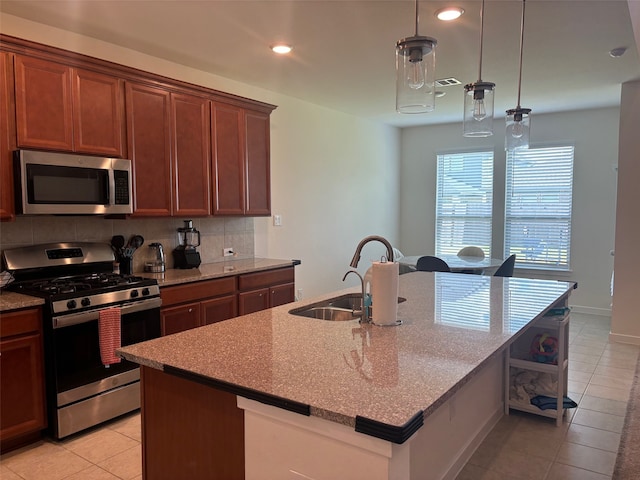 kitchen with light stone counters, an island with sink, pendant lighting, decorative backsplash, and appliances with stainless steel finishes