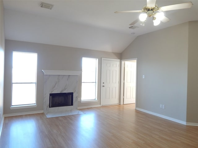 unfurnished living room with lofted ceiling, a high end fireplace, ceiling fan, and light hardwood / wood-style flooring