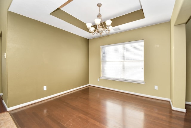 unfurnished room with dark hardwood / wood-style flooring, a tray ceiling, and an inviting chandelier