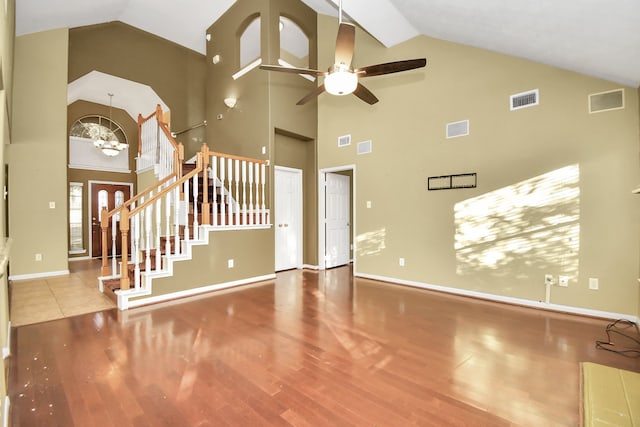 unfurnished living room with wood-type flooring, ceiling fan with notable chandelier, and high vaulted ceiling